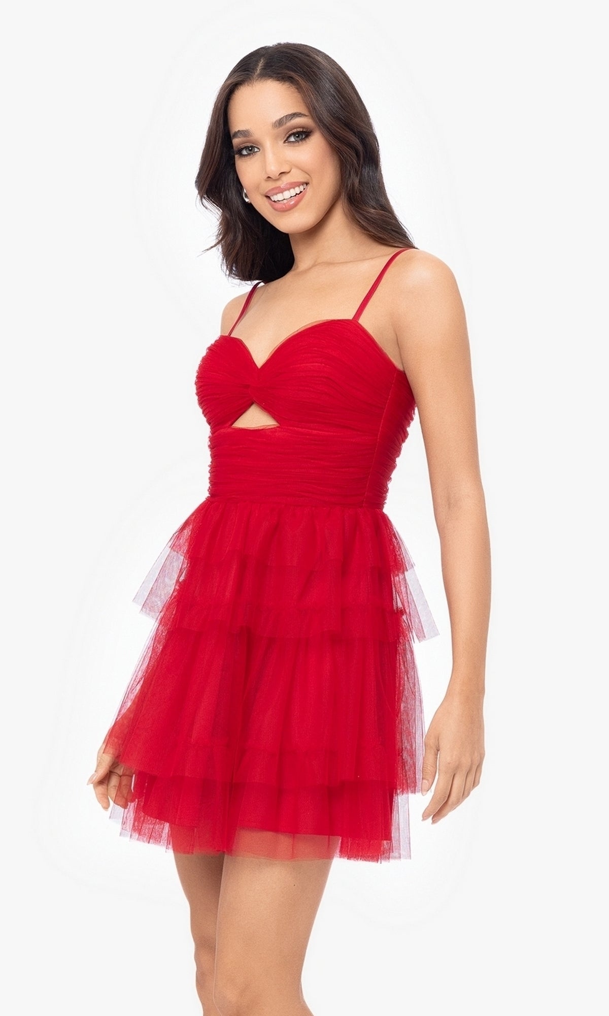 A woman models the Cut-Out Short Ruffled Homecoming Dress 5098BN—sleeveless, red tulle with thin straps, ruched sweetheart bodice, front cutout, and a short ruffled A-line skirt—against a plain white background.